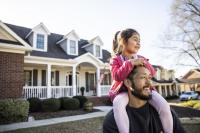 Un homme porte une petite fille sur ses épaules devant une maison. 