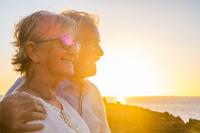 Un homme senior et une femme senior sourient en regardant la mer au soleil couchant