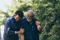 Un homme serre son père âgé dans ses bras. Ils sourient et marchent dans un parc.