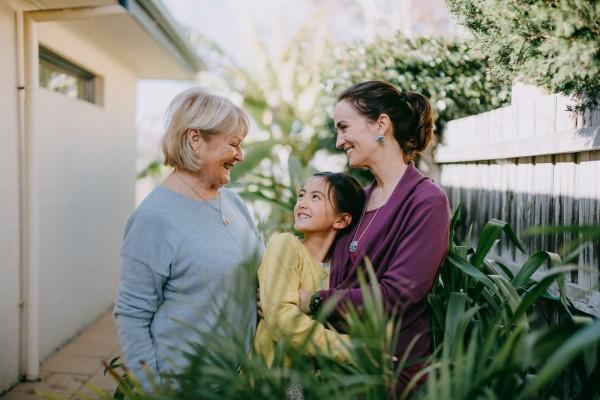 Trois générations de femmes en train de se sourire dans un jardin.