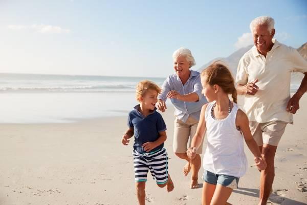 Des grands-parents courent sur une plage avec leurs petits-enfants