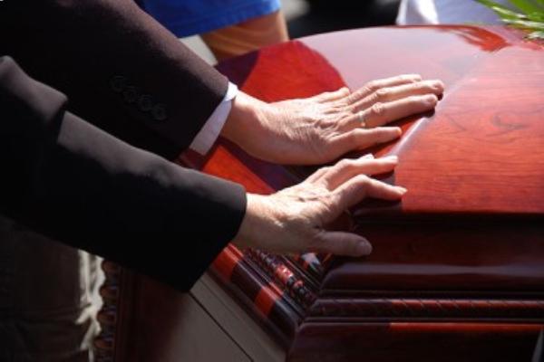 La main d’un homme et la main d’une femme posées sur un cercueil