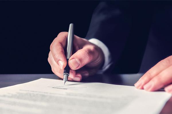 Main d'un homme qui tient un stylo à plume et signe un testament