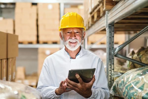 Un quinquagénaire avec un casque de sécurité dans un entrepôt avec une tablette à la main