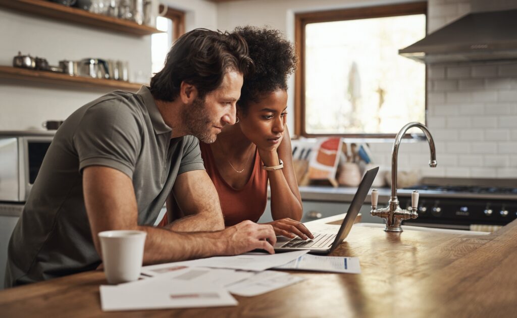 Ordinateur portable, couple et planification financière dans une cuisine avec des documents pour le budget, l'épargne et le paiement des factures.