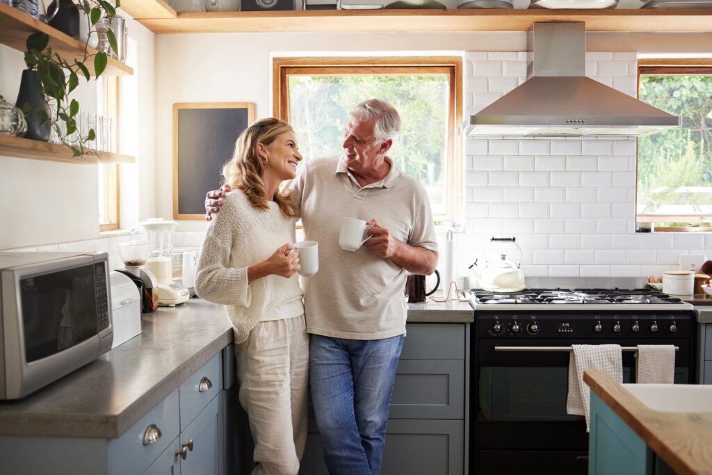 Les personnes âgées, couple et boire du café avec l'amour, le mariage et l'état d'esprit matinale de bonheur à la maison. Le sourire heureux et l'étreinte d'une femme et d'un homme âgés avec du thé dans la cuisine d'une maison ensemble avec du temps de qualité.