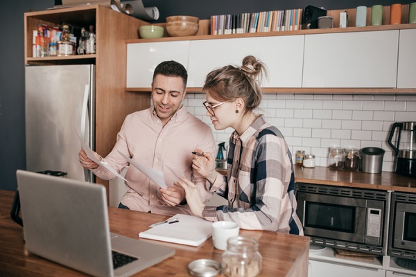Un couple debout dans leur cuisine, discute projet devant leur ordinateur posé sur la table